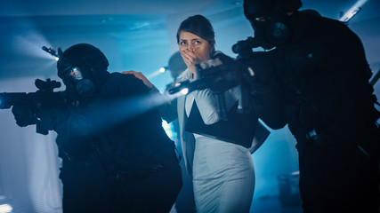 Masked Squad of Armed SWAT Police Officers Rescue a Female Hostage in a Dark Seized Office Building with Desks and Computers. Soldiers with Rifles and Flashlights Move Forwards and Cover Surroundings.