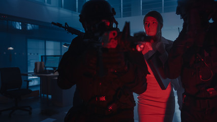Masked Squad of Armed SWAT Police Officers Rescue a Female Hostage in a Dark Seized Office Building with Desks and Computers. Soldiers with Rifles and Flashlights Move Forwards and Cover Surroundings.