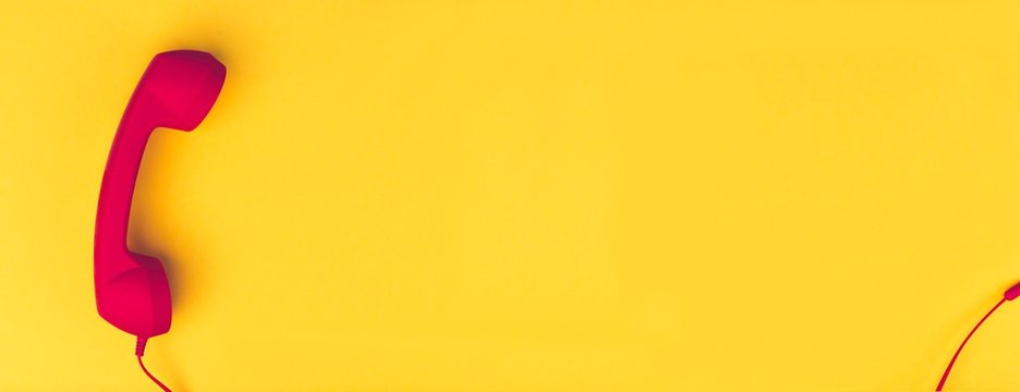 Red landline telephone receiver  in front of yellow background. Panoramic image with copy space. 