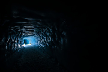 Blue Light at the end of a tunnel. Beautiful textured ice walls are visible in an ice cave inside a Glacier in Iceland. These caves can be explored by the adventure enthusiasts in the winter months