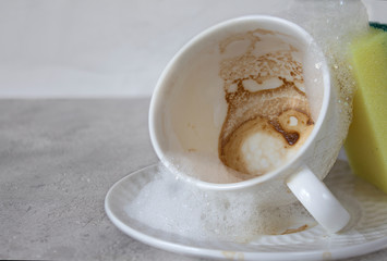 A dirty coffee Cup on a gray background. The selected focus. Coffee foam close-up. Sponge and foam for washing dishes. Copy space. Guessing on coffee