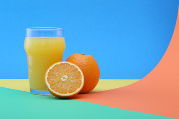 Glass of orange juice and oranges on a colorful background