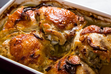 Baked chicken thighs with onions in ceramic form on a stone table, copy space.