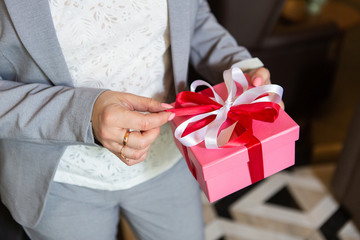 Hands of a woman in a business suit holding a gift box with a red bow.and a close-Up of hands with a gift box. Business lady at a gift presentation