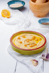 Bowl of arabic or lebanese vegetarian hummus.in green bowl on a white wooden background. Traditional Middle eastern hummus. Healthy eating concept,