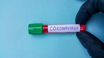 Obraz premium Coronavirus Covid-19 Vacuum Tubes For Medical Work With Blood Samples In The Laboratory. Coronavirus Test. A doctor's hand in a black rubber medical glove. Space for text on a blue background.