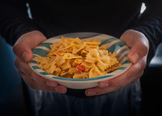 Pasta with minced chicken in a deep striped light cup with blue stripes in the hands of a young man