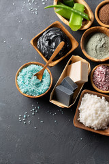 Fototapeta na wymiar Spa. Natural cosmetics for the body and face. Blue sea salt with seaweed, soaps of herbs and dead sea mud, ground coffee scrub, aloe vera, clay for face mask on a dark table. Top view. Copy space.
