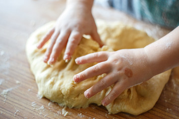 Child's hands knead yeast dough closeup
