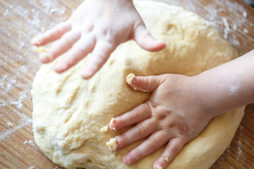 Child's hands knead yeast dough closeup