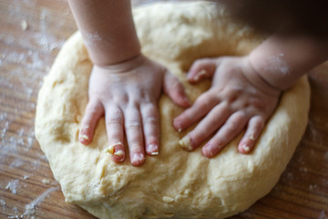 Child's hands knead yeast dough closeup