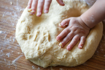 Child's hands knead yeast dough closeup