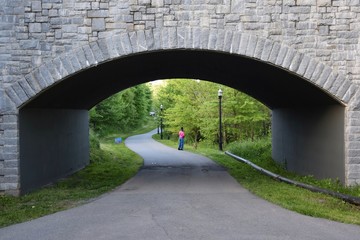 Obraz premium Park landscape and a pedestrian walkway underneath a bridge with stone exterior