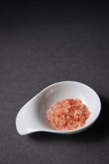 Closeup of Himalayan salt in white bowl on dark gray background. Macro, vertical.