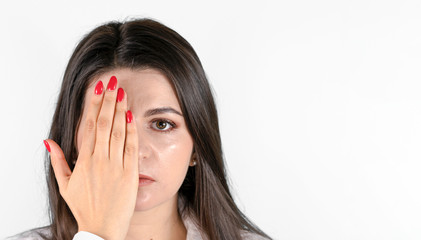 Young brunette woman   covering one eye with her hand and looking at camera. Front portrait against gray background with copy space