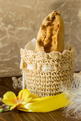 The image shows a typical Easter panzerotto from Campania inside a beige crochet basket with yellow and white feathers on dark wood and gray background