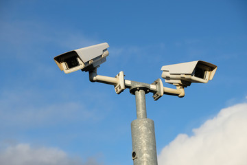 Two Closed Circuit security cameras (CCTV) with a background of a blue sky. Concept of security, surveillance, being watched