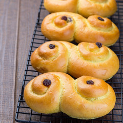 Swedish and scandinavian Christmas saffron buns Lussekatter on cooling tray, brown wooden background, square format