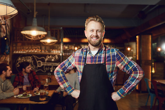 Bearded smiling barman waiter standing on the background of a bar.