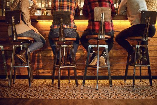 Rear view friends sitting on chairs talking at the bar in a bar.
