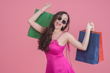 Portrait of asian woman holding bags and standing over pink background. Half  length of a happy pretty girl holding shopping bags in hand.