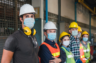 Group of diverse team of workers wearing face mask and protective helmets standing in front of the factory