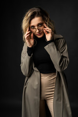 Beautiful girl wearing a casual trendy trousers, turtleneck glasses and raincoat posing on a dark background. Fashionable, advertising, lifestyle and commercial design.