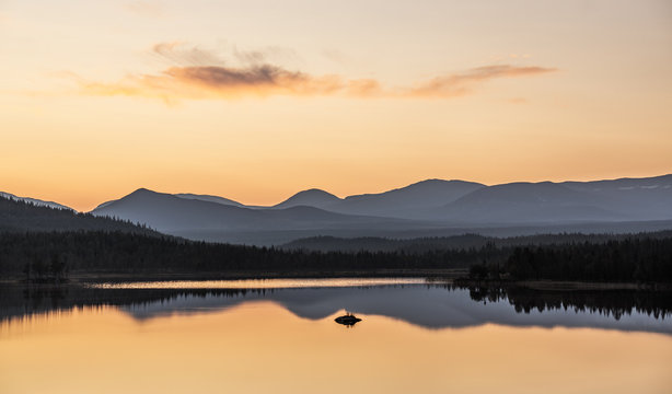 colorful sunset in sweden over a mountain range with still lake in foreground and clean reflections during golden hour in late summer