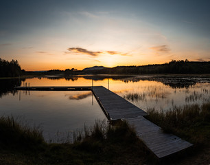 warm sunset over a pier in sweden with clouds and reflections in the lake