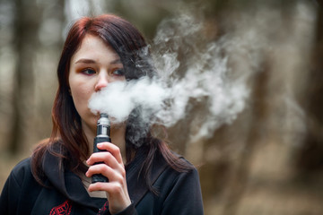 Vape teenager. Young pretty caucasian brunette girl smoking an electronic cigarette on the street...