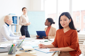 Portrait of elegant Asian businesswoman looking at camera while sitting at table in office during business meeting, copy space