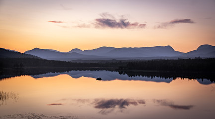 Naklejka na ściany i meble colorful sunset in sweden over a mountain range with still lake in foreground and clean reflections during golden hour in late summer