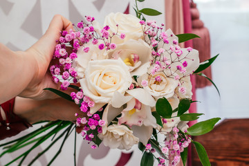 The florist's hands hold the bouquet of cream roses,orchid,ruskus leaves, pink gypsophila  in the process of making it