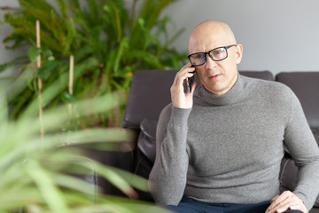 A man is sitting on a sofa with a phone at home. Epidemic. Isolation and communication.