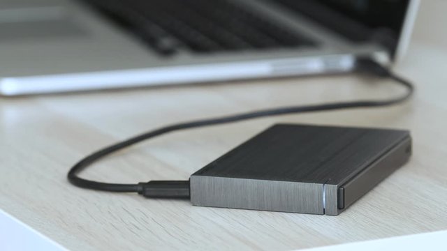 External Hard Drive On a Table, Led Light Flickering, Laptop Computer in the Background - Solid Aluminium Casing HDD, Minimalist Design Composition - Macro Closeup
