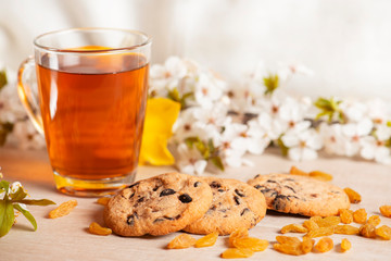 Morning breakfast. Cup of tea , raisin,  cookies with chocolate on the wooden background and spring flowers.

