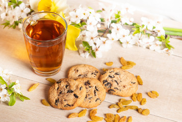 Morning breakfast. Cup of tea , raisin,  cookies with chocolate on the wooden background and spring flowers.
