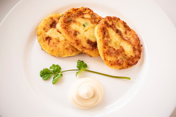 Potato pancakes on a white plate with sauce and a sprig of coriander
