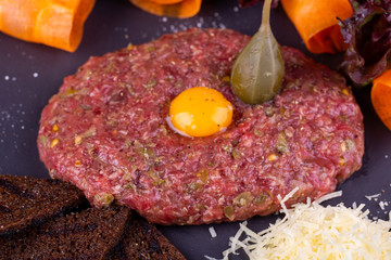 Meat tartar with quail egg, served with grated cheese, rye bread chips and vegetables