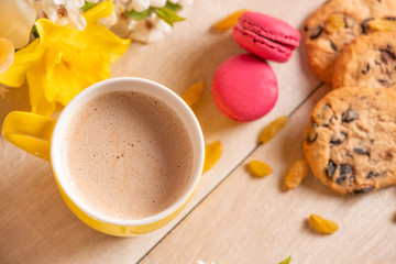 Morning breakfast. Cup of cappuccino, cookies with chocolate, red macaroons and grape raisin on the wooden background and spring flowers.
