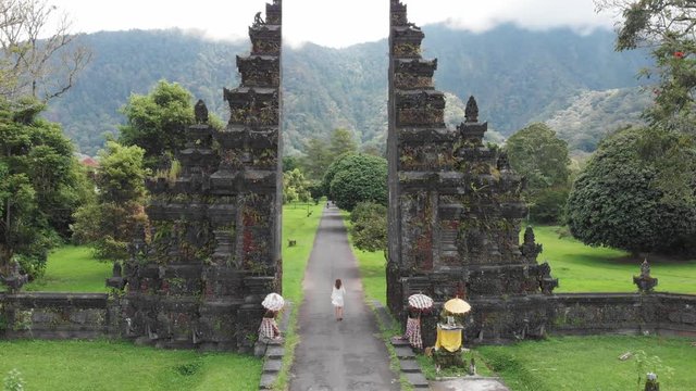 Unrecognizable tourist woman running through bali traditional gate in bedugul Traditional Balinese Hindu gate Candi Bentar close to Bedugul, Bratan lake, Bali island, Indonesia