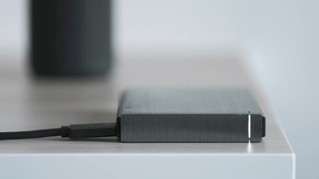 External Hard Drive On a Table, Led Light Flickering, Bluetooth Speaker in the Background - Solid Aluminium Casing HDD, Minimalist Design Composition - Macro Closeup