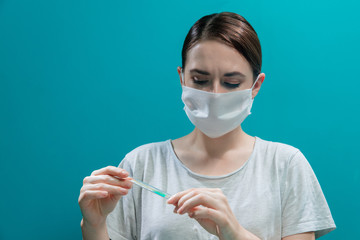 a girl in a medical mask holds a thermometer in her hands and looks at it