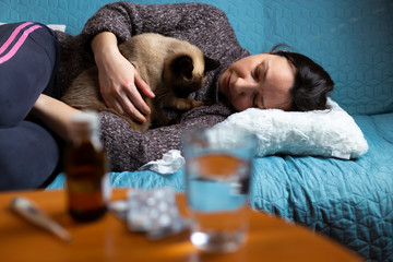 Woman feeling sick sitting on couch with her cat in her arms