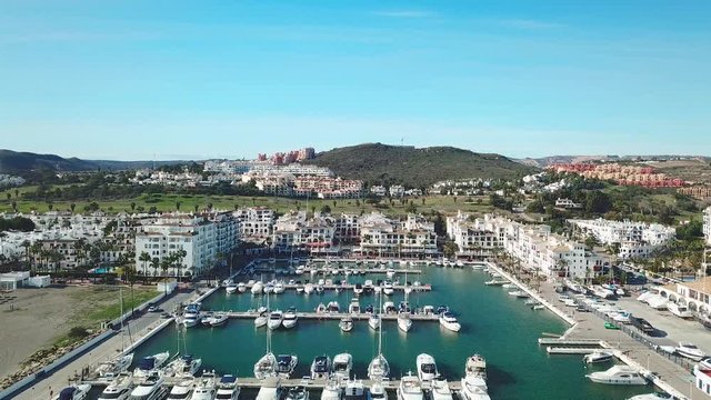 Beautiful Aerial panoramic view of "Puerto de la Duquesa" in MANILVA- Malaga SPAIN. Yachts and boats docked in the Harbour. Luxury Apartment Urbanisation and Restaurants . Dolly in and pedestal down