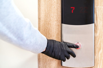 A man in black protective gloves presses the Elevator button during an epidemic of coronavirus and infectious diseases. Preventive measures to reduce the spread of the flu virus. Soft focus.