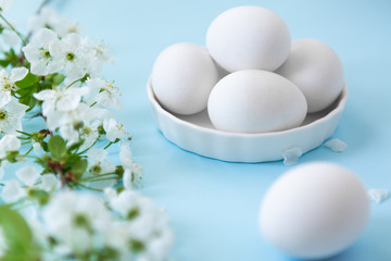 White eggs in bowl on blue background with flowers