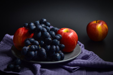 Grapes and red apples on a plate on a black background.