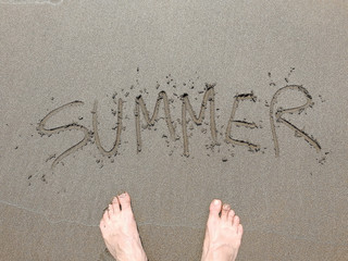 The word summer on the sandy beach and the men's feet. the concept of leisure holiday