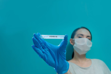 A girl in a medical mask and blue gloves shows a test tube with the virus